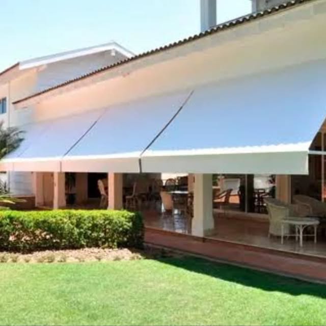 Toldos brancos ao longo de uma varanda diante de um jardim